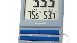 Digital thermohygrometer displaying temperature and humidity readings with a visible alarm indicator and control buttons.