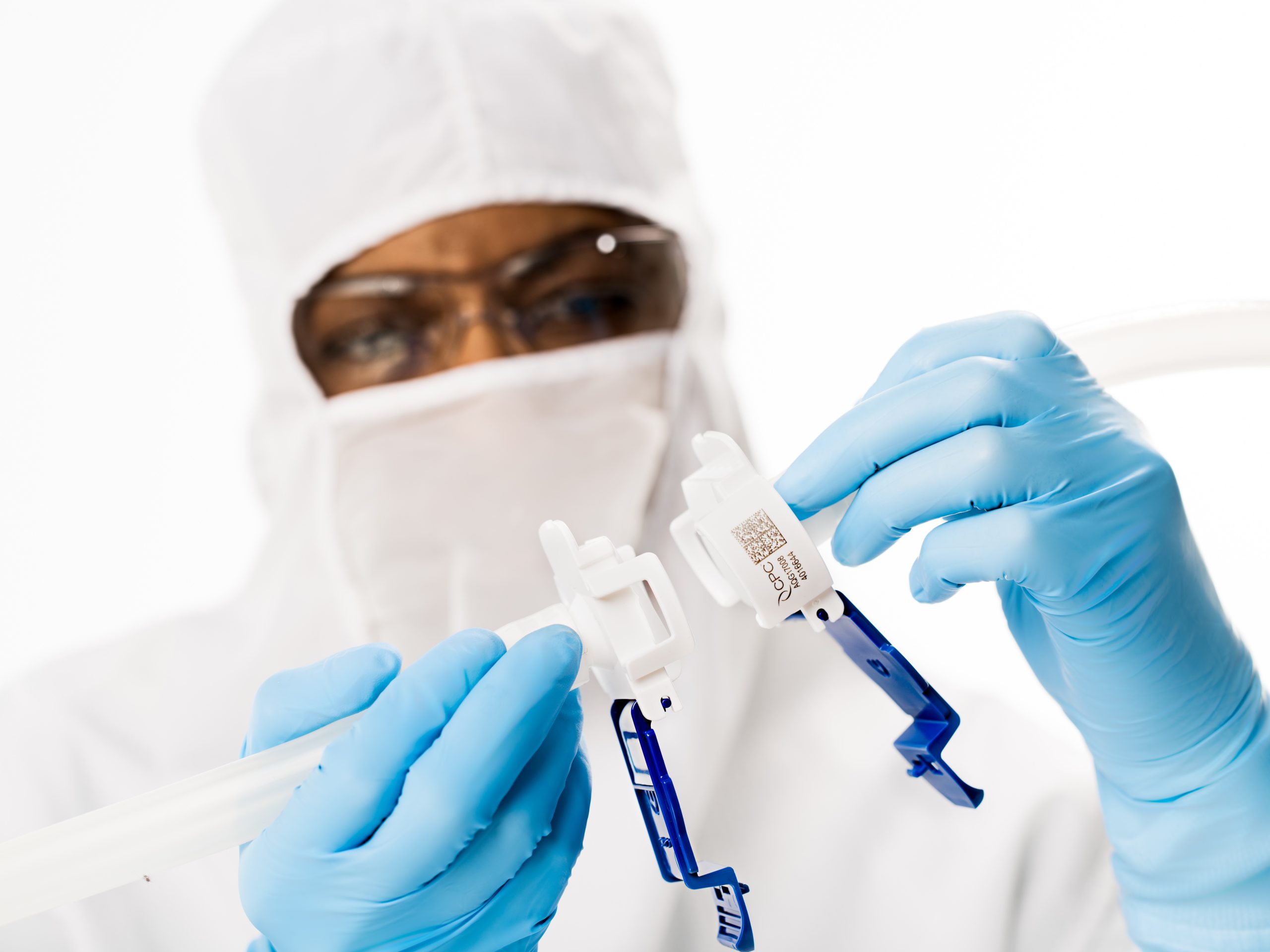 Scientist in cleanroom attire handling AseptiQuik connectors, demonstrating sterile connection of tubing components with precision.