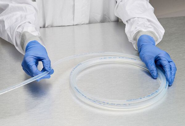 Gloved hands holding clear braided tubing on a stainless steel surface, highlighting its use in cleanroom environments.